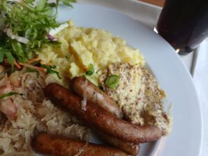 nuernberger wuerstchen mit dijon senf dip sauerkraut mit petersilie und pink lady auf kartoffelstampf mit glas malzbier